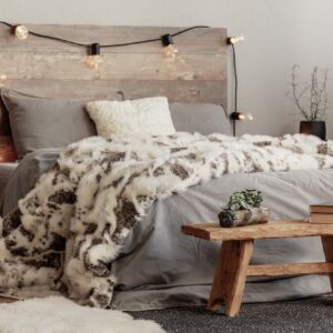 Wooden bench in the foot of the bed with grey bedding and cozy blanket